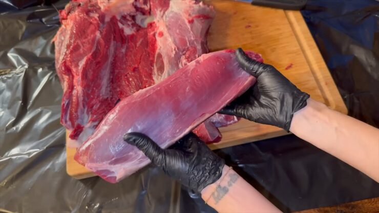 Freshly removed deer eye of round muscle held by hand after separation from the hind quarter during butchering